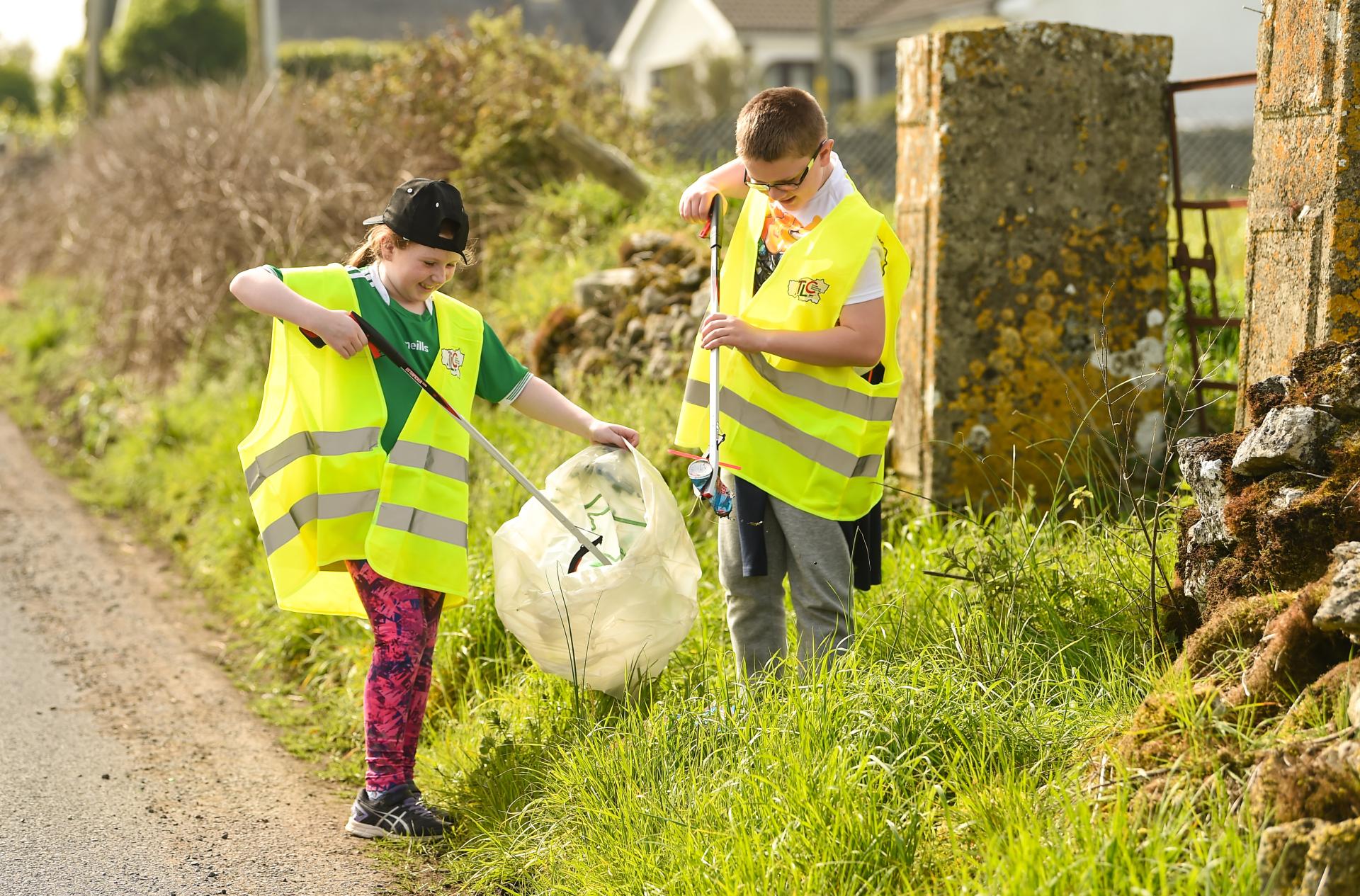 A girl and boy tidy up on the side of a road